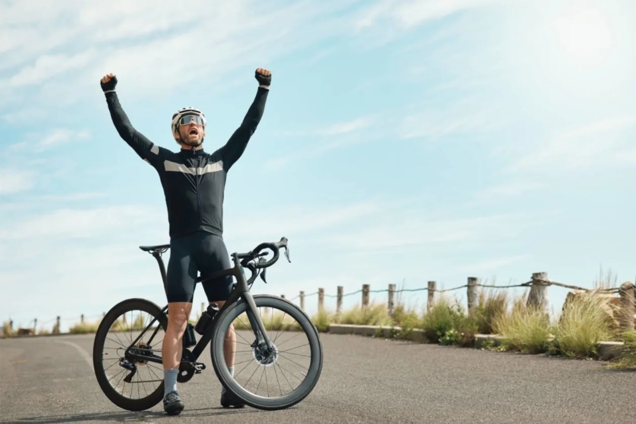 Full length shot of man standing over bike with arms raised